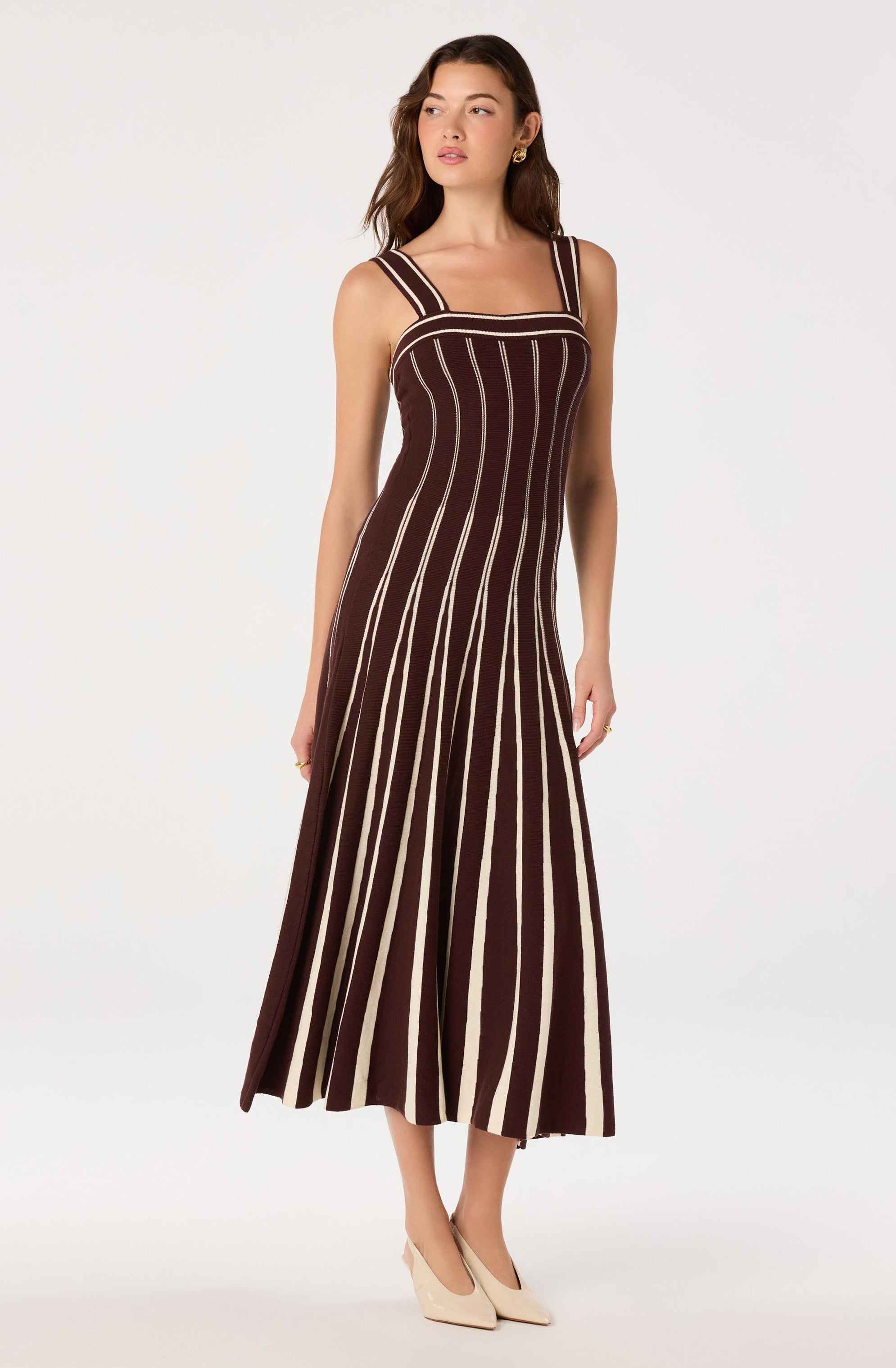 Woman wearing a sleeveless brown dress with vertical beige and white stripes.