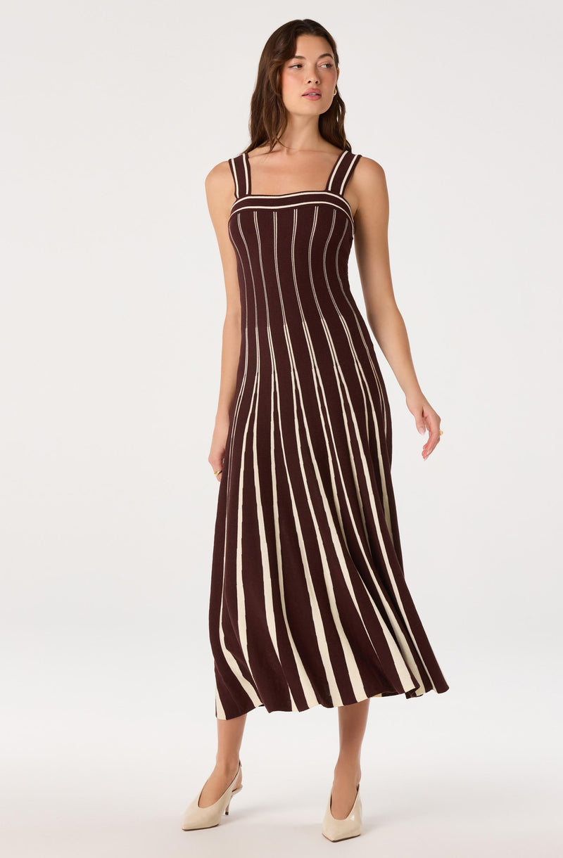 Woman wearing a sleeveless, striped, floor-length dress with dark and cream vertical lines.