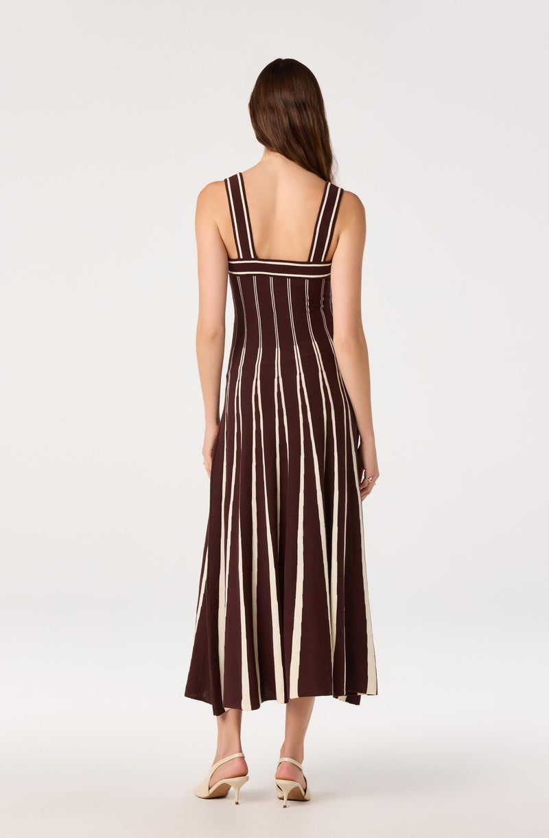 Girl wearing a sleeveless, brown dress with vertical white and beige stripes, and open-toe heels.