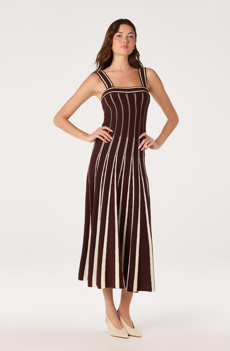 Woman wearing a sleeveless, wide-strap, maroon and cream striped jumpsuit with a fitted waist.