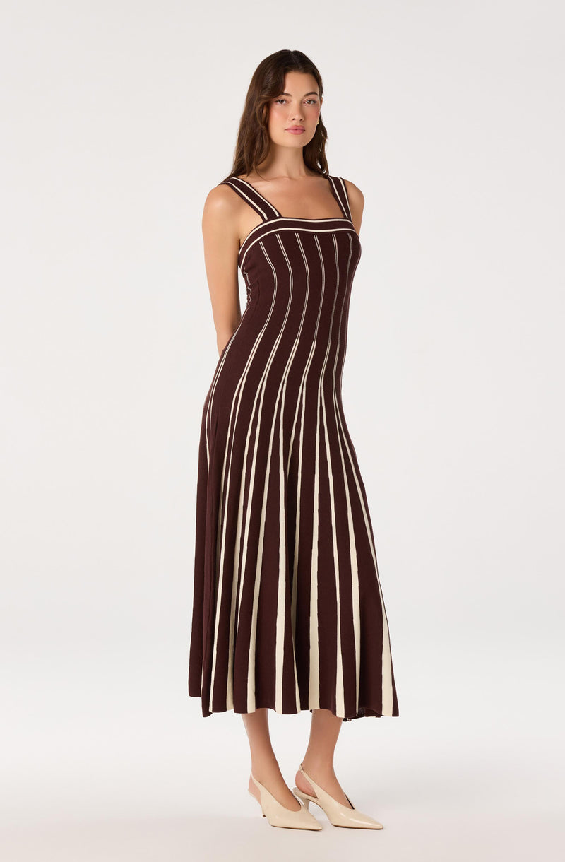 Woman wearing a brown and beige striped sleeveless, ankle-length dress with wide shoulder straps.
