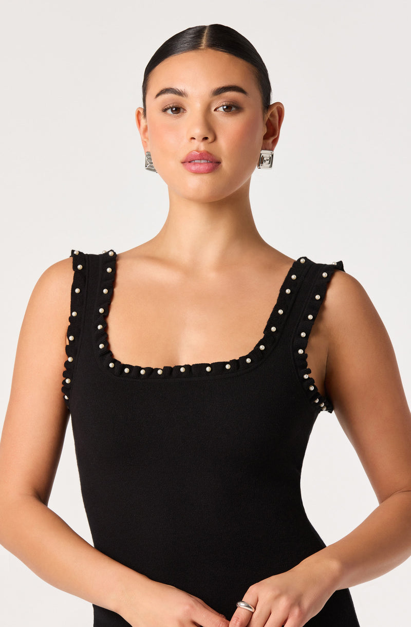 Woman in black sleeveless top with pearl-embellished straps and neckline.