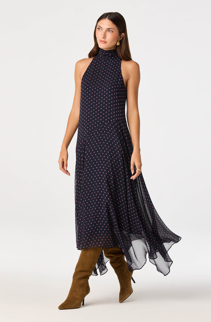 Woman in navy polka dot sleeveless dress with high neckline, paired with tan knee-high boots.