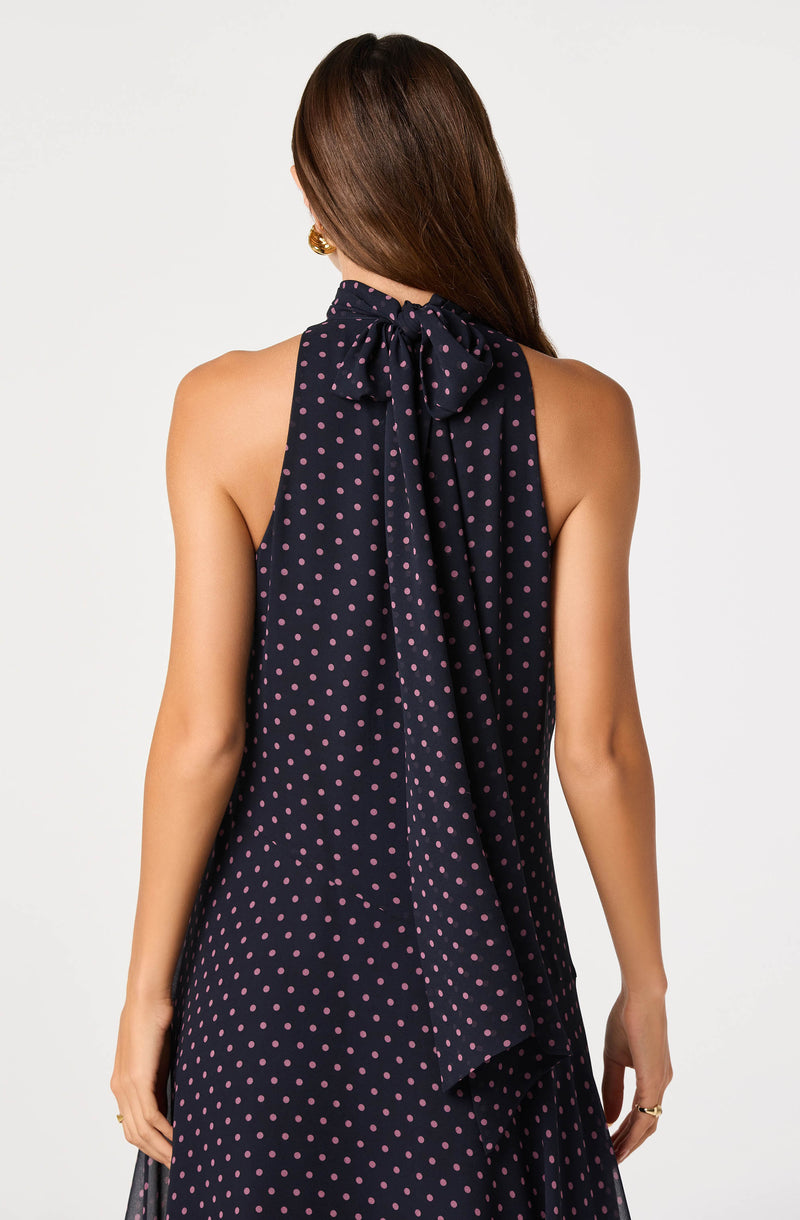 Back view of a woman wearing a navy dress with pink polka dots and a large bow tie at the neck.