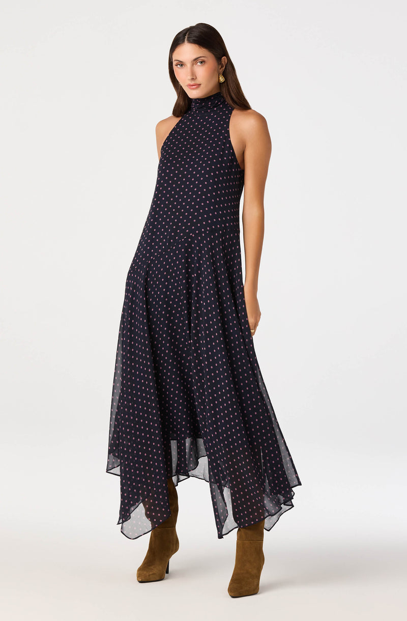 Woman wearing a sleeveless, high-neck navy dress with pink polka dots and an asymmetrical hemline.