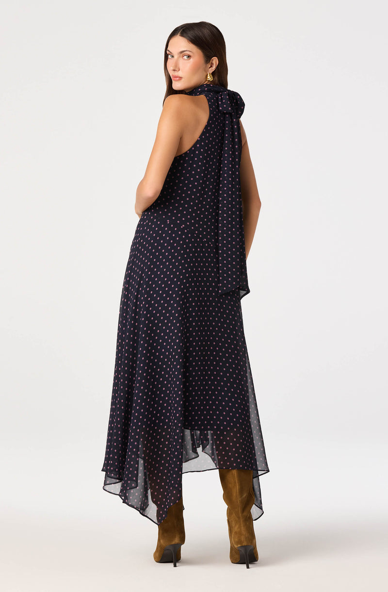 Woman wearing a navy blue dress with pink polka dots and a large bow at the back.