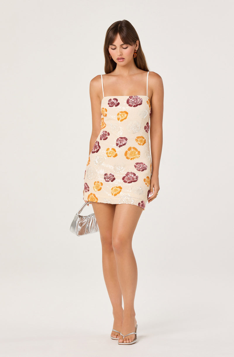 Girl in a white dress with colorful floral patterns, thin spaghetti straps, and a metallic silver handbag.