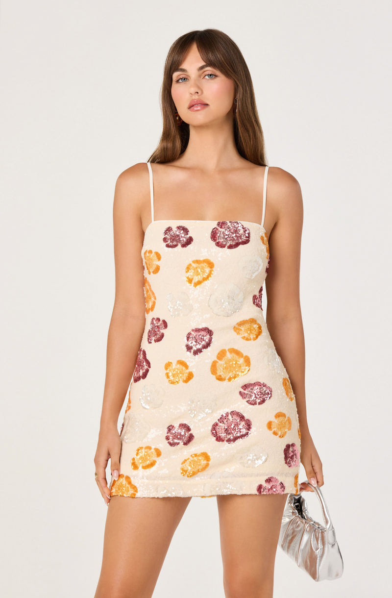 Girl in a cream-colored dress with pink, orange, and white floral sequined patterns, thin shoulder straps, holding a small silver handbag.