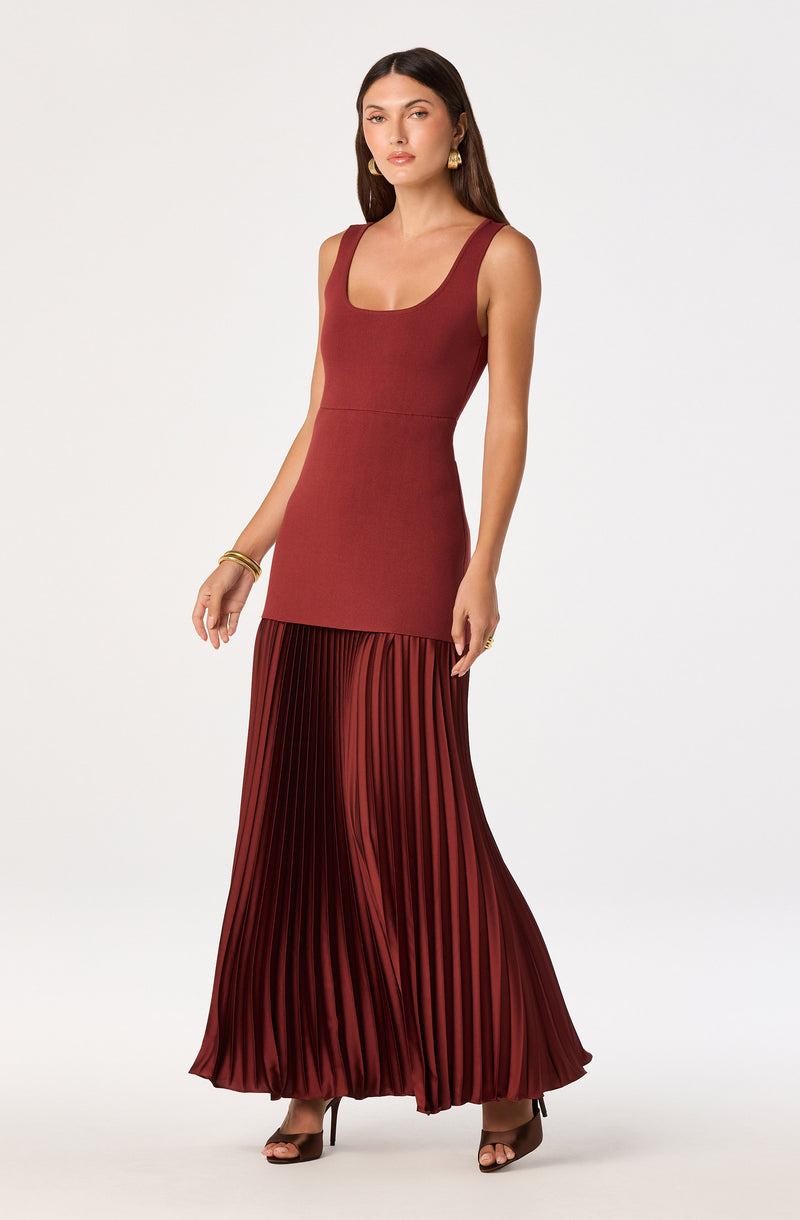 Woman in a sleeveless, fitted, brick-red top with a pleated, matching floor-length skirt.