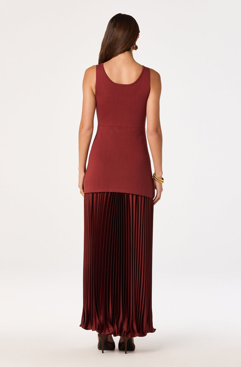 Woman in a sleeveless, fitted, rust-colored top and a long, pleated, maroon skirt.