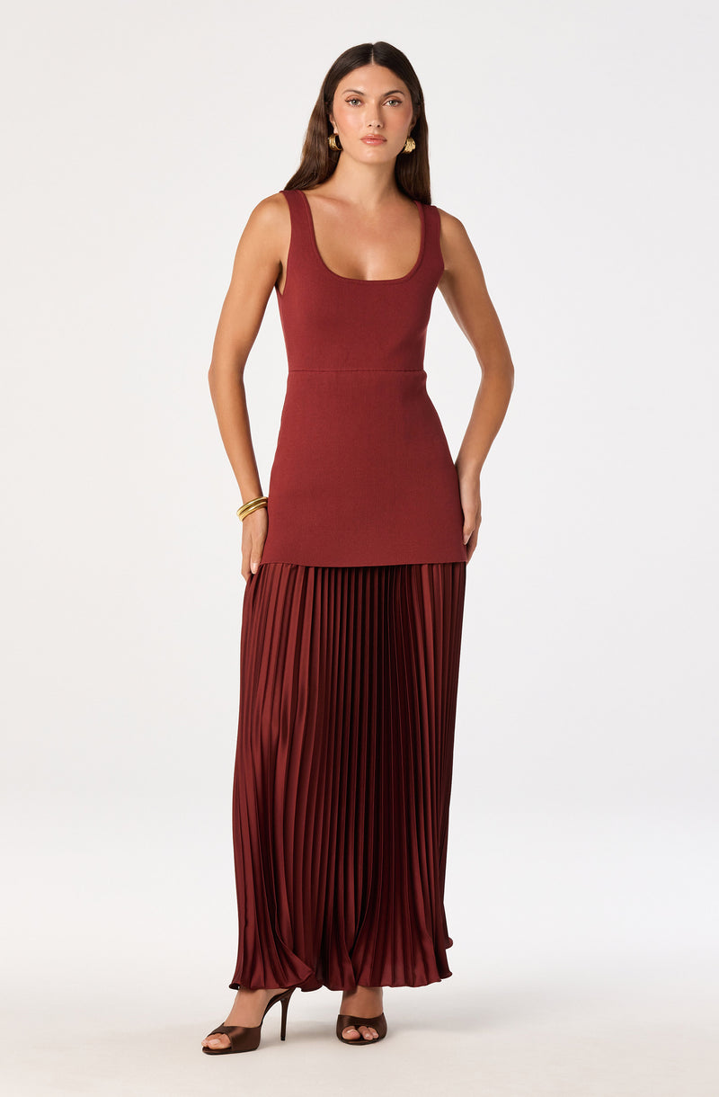 Woman in a sleeveless, maroon top with a pleated, satin-like maroon maxi skirt and high heels.