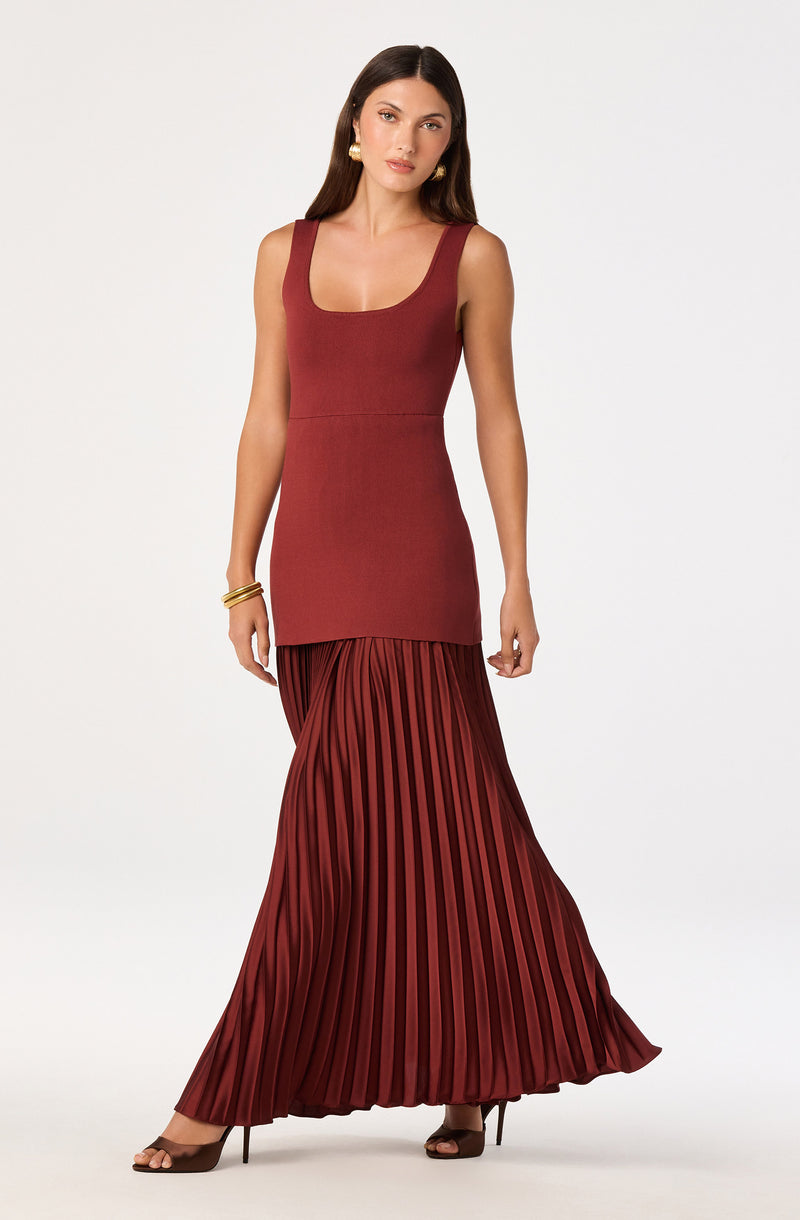 Woman in a sleeveless, rust-colored top and a long, pleated, matching skirt.