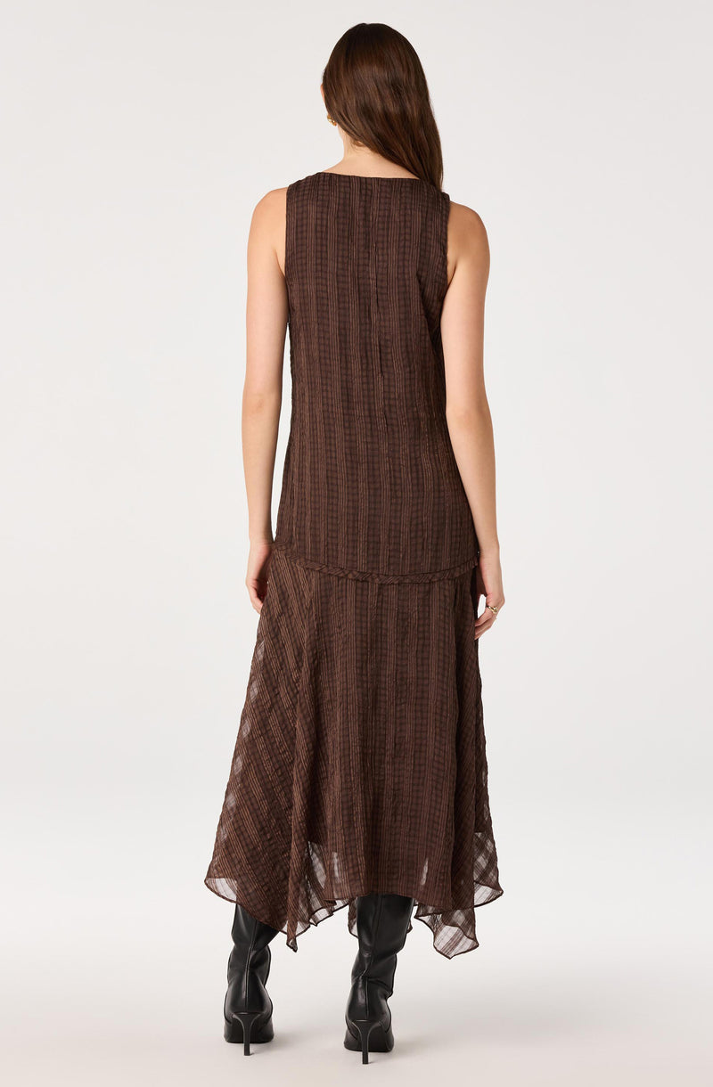 Woman in a sleeveless, brown striped mesh dress with an asymmetrical hem, wearing black knee-high boots.