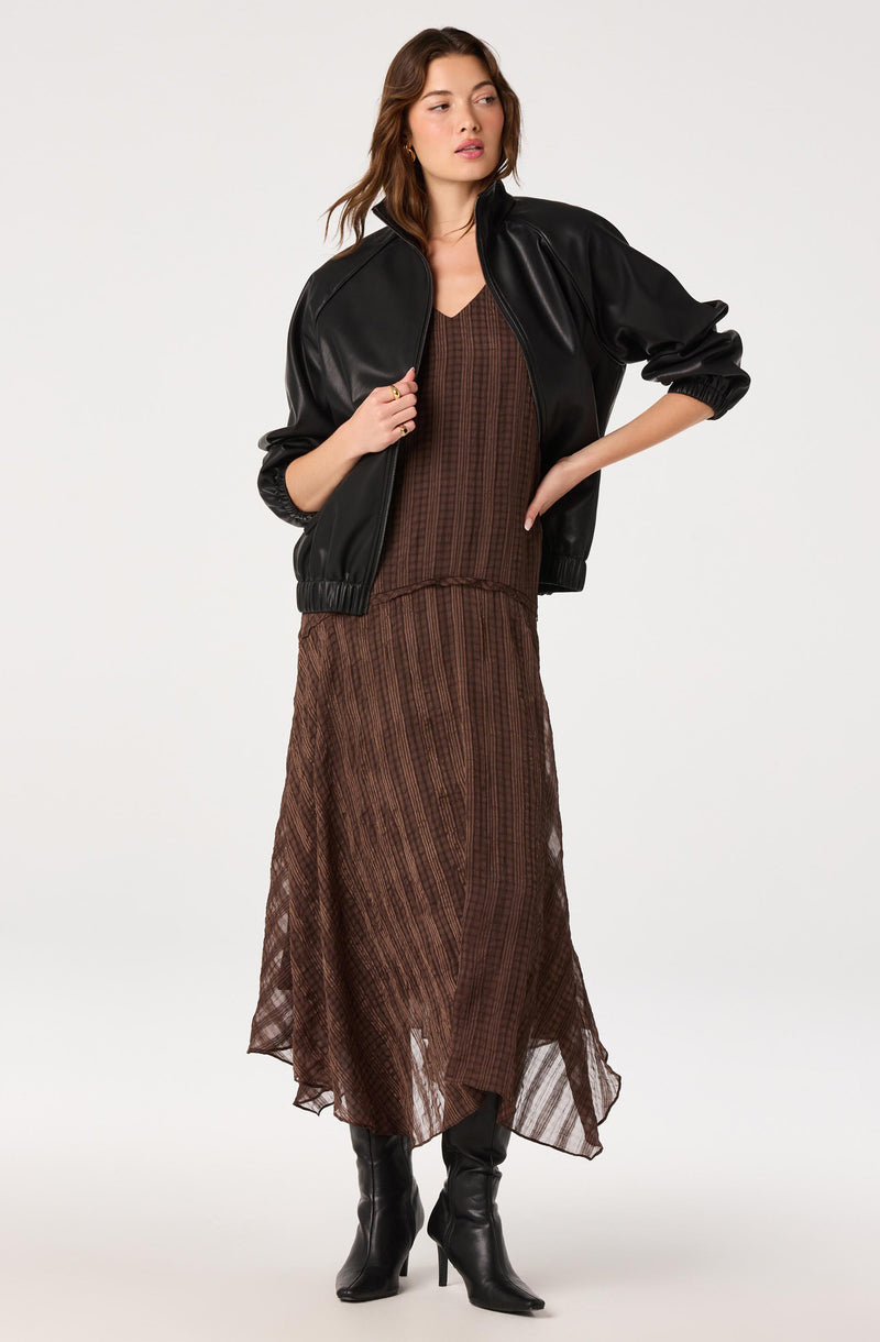 Woman wearing a black leather jacket, brown striped dress, and black high-heeled boots.