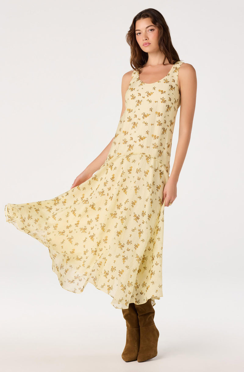 Woman in a sleeveless, cream-colored dress with a yellow floral pattern, paired with brown knee-high boots.