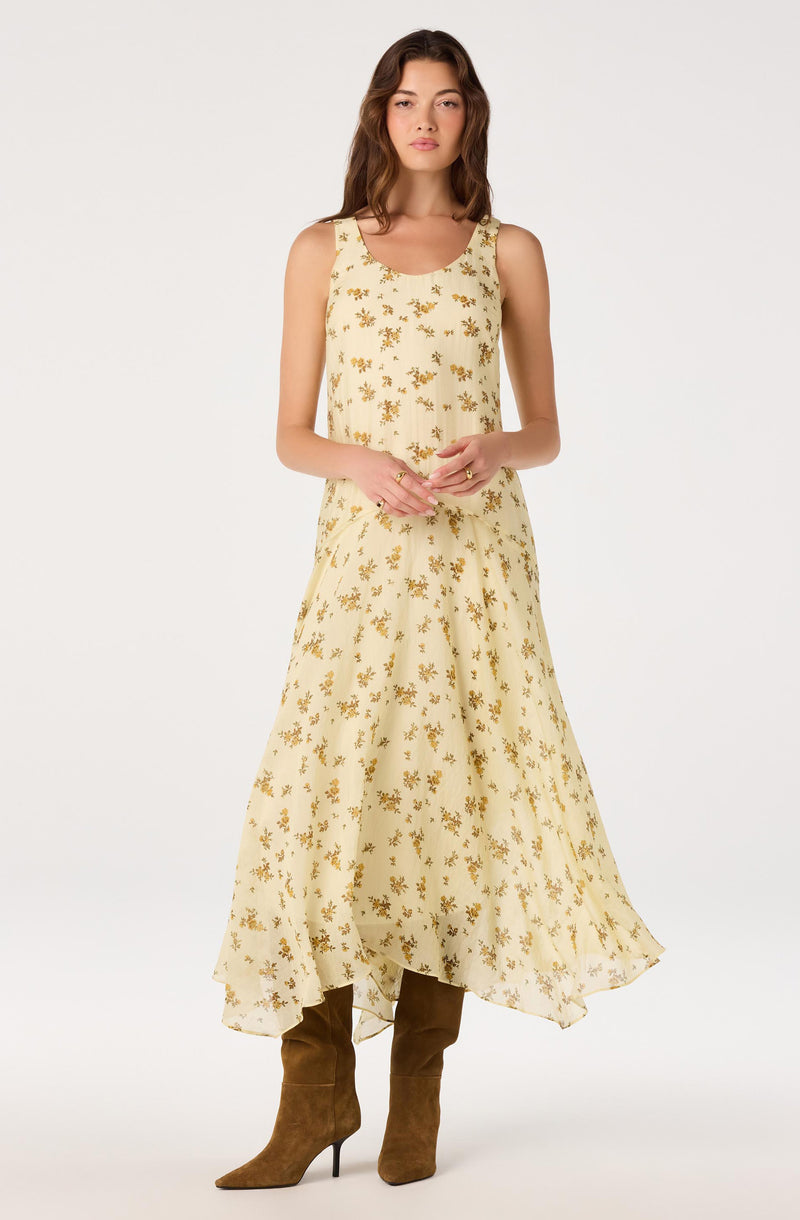 Woman wearing a sleeveless, cream-colored dress with small yellow floral print and brown knee-high boots.