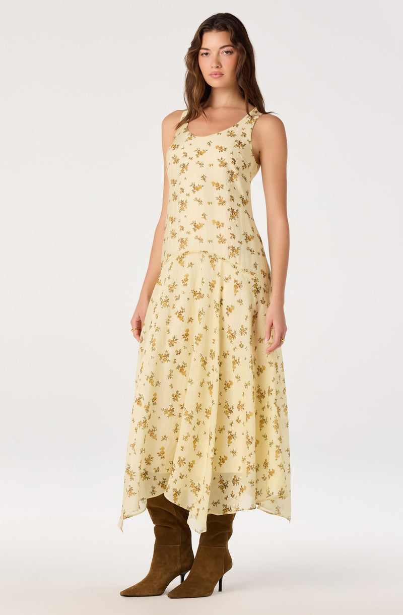 Woman in a sleeveless, ankle-length, cream dress with yellow floral pattern, paired with brown high-heeled boots.