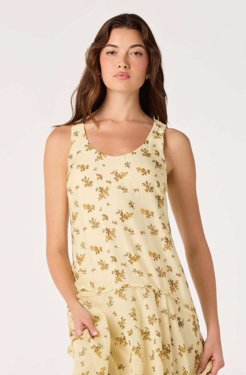 Woman in a cream sleeveless dress with a yellow floral pattern.