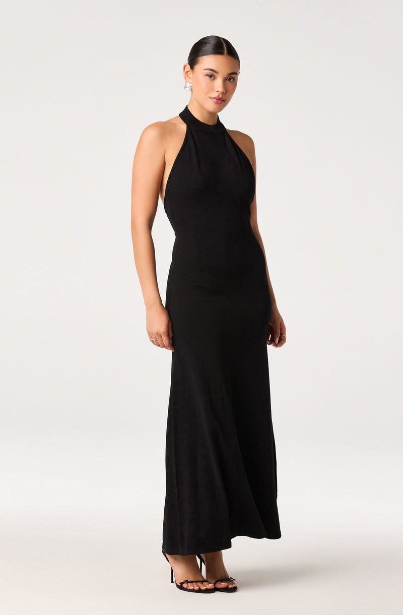 Woman wearing a sleeveless, high-neck, floor-length black dress with open shoulders.