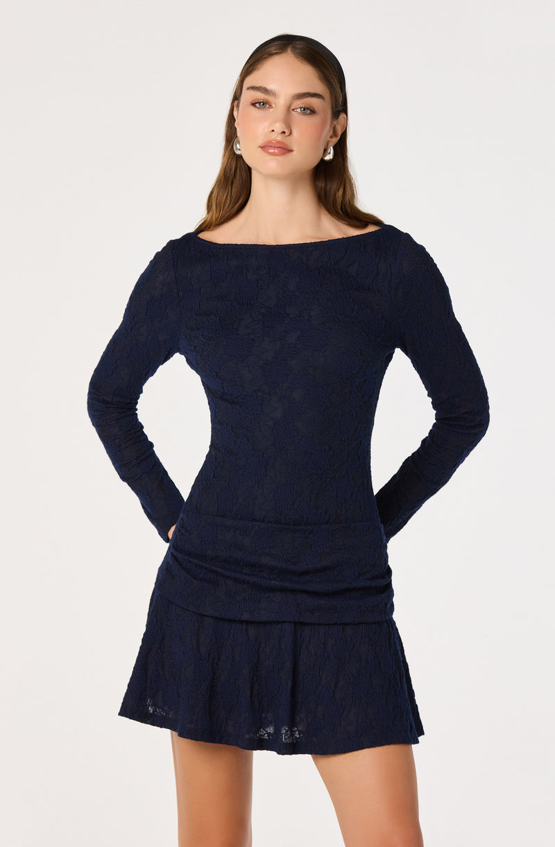 Woman wearing a dark navy long-sleeve lace dress with a round neckline and a layered skirt.