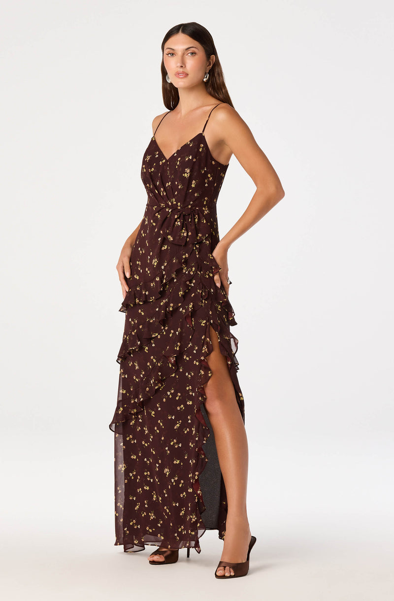 Woman in a dark brown, ruffled, floral maxi dress with spaghetti straps and high slit.