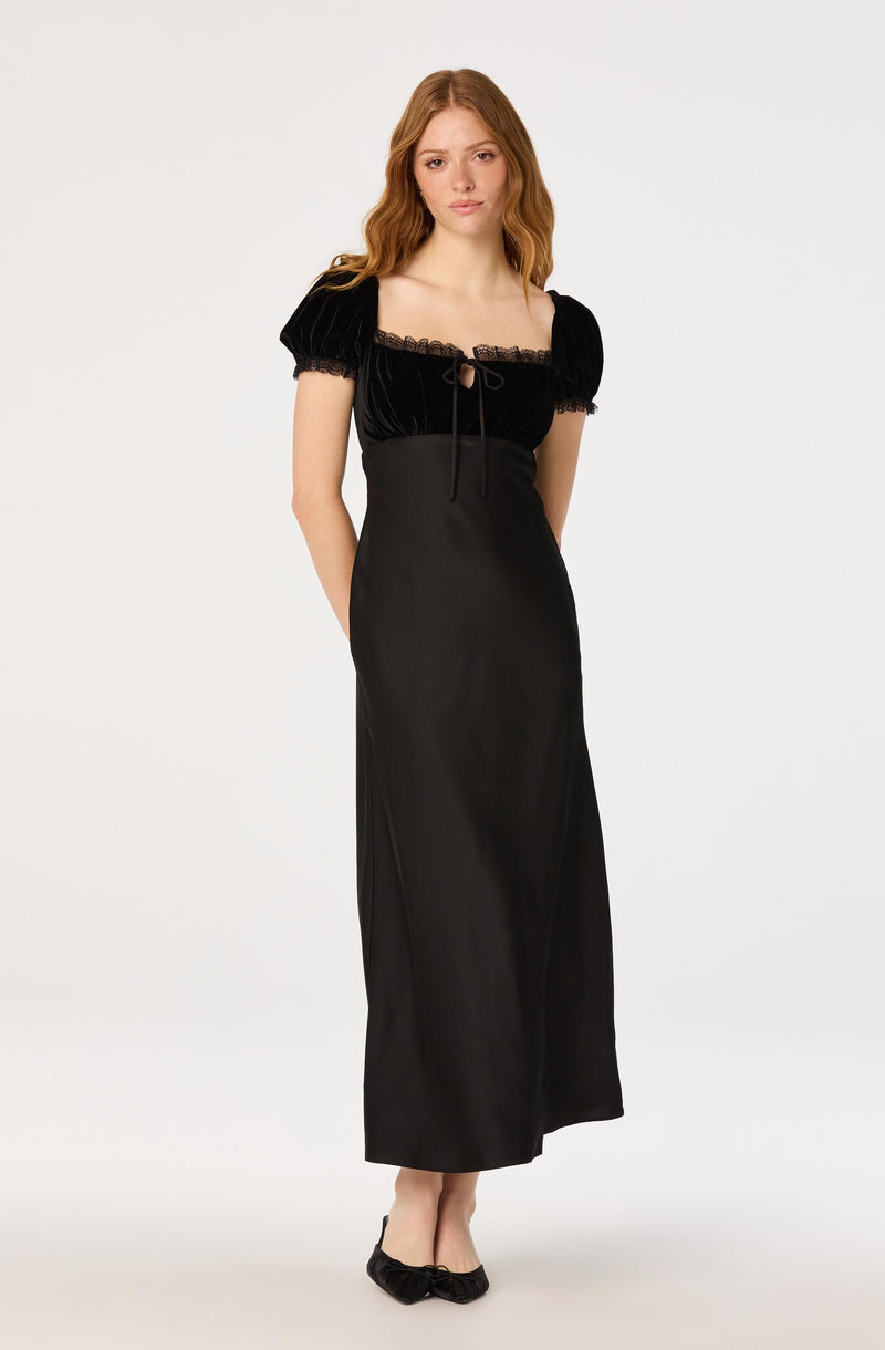 Young woman in a black dress with puff sleeves, lace trim, and a floor-length skirt, paired with black flats.