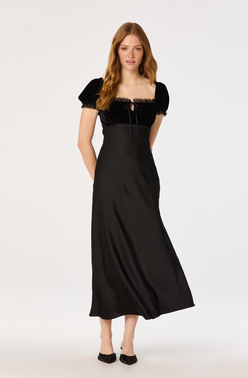 Woman wearing a black dress with puff sleeves and a lace neckline, paired with black bow shoes.