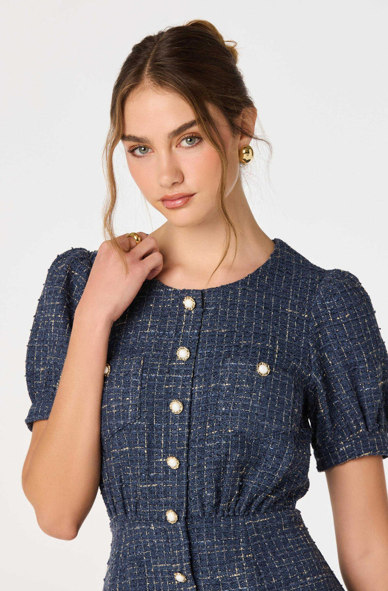 Woman in navy tweed dress with gold buttons and puffed short sleeves.