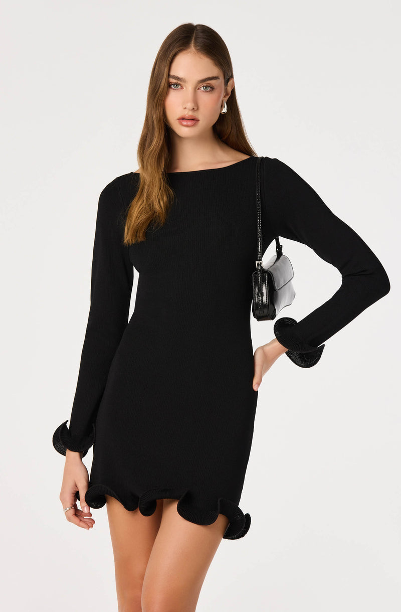 Woman wearing a black long-sleeve dress with ruffled cuffs and hem, carrying a small black and white purse.