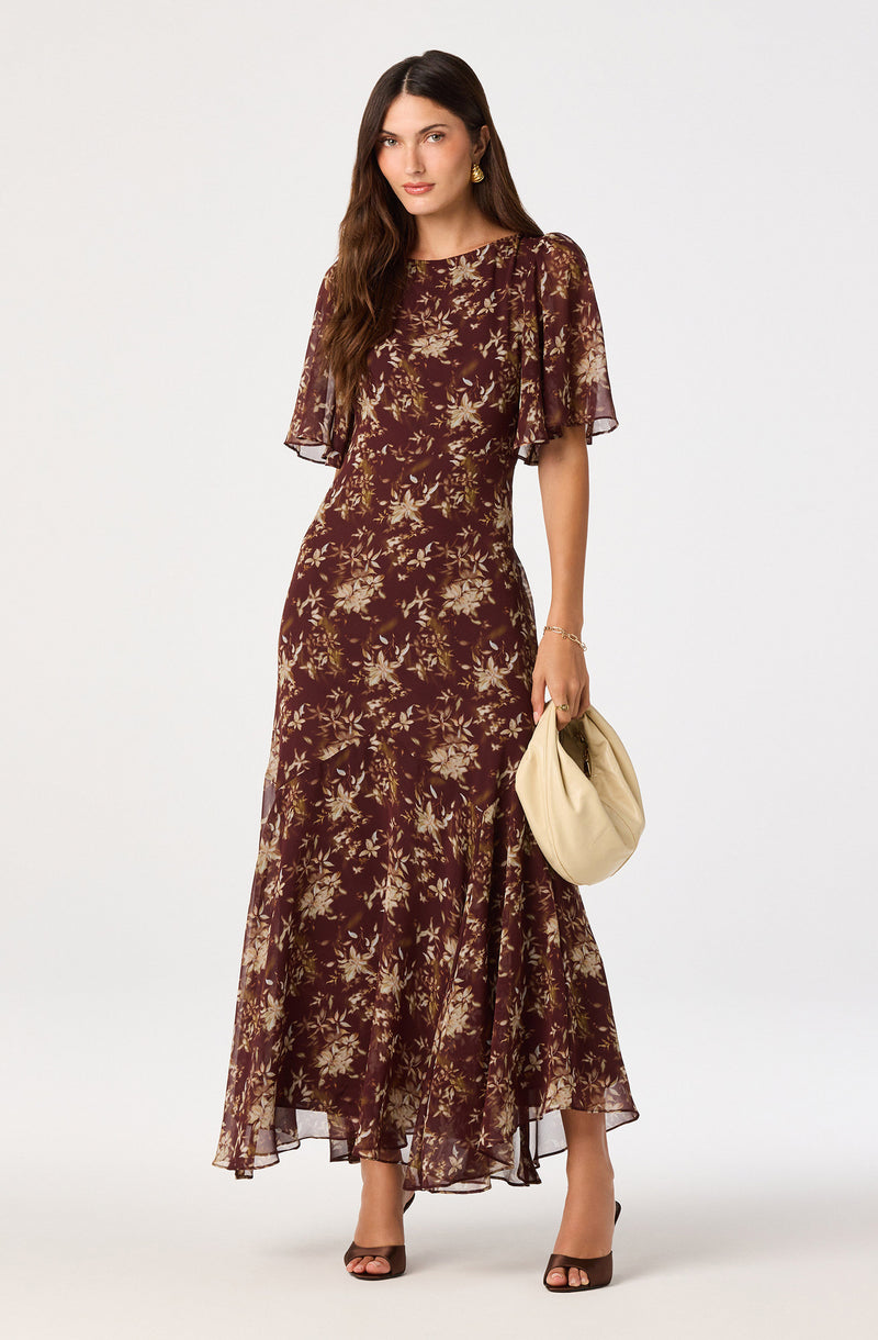 Woman wearing a long, floral-patterned dress with sheer, ruffled short sleeves and black open-toe heels.