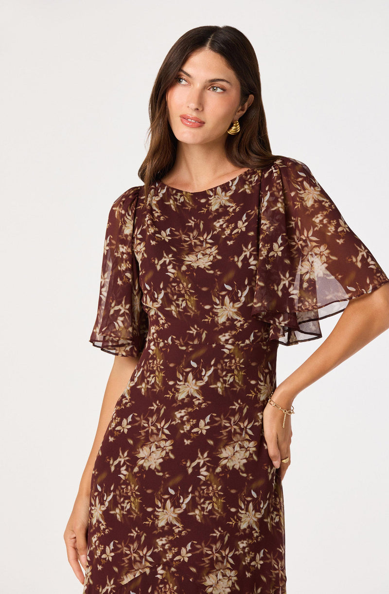 Woman wearing a dark floral dress with sheer, puffed sleeves and a fitted waist.