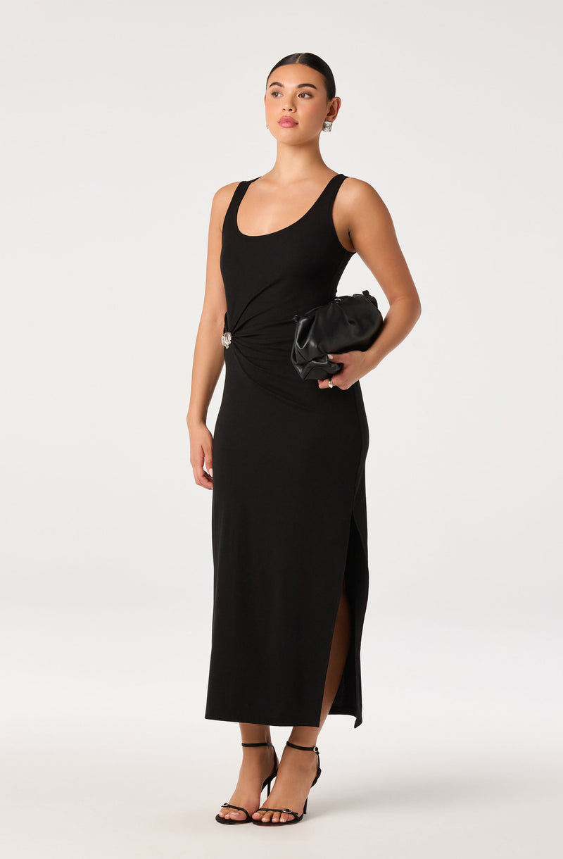 Woman in a black sleeveless dress with a slit, holding a black clutch.