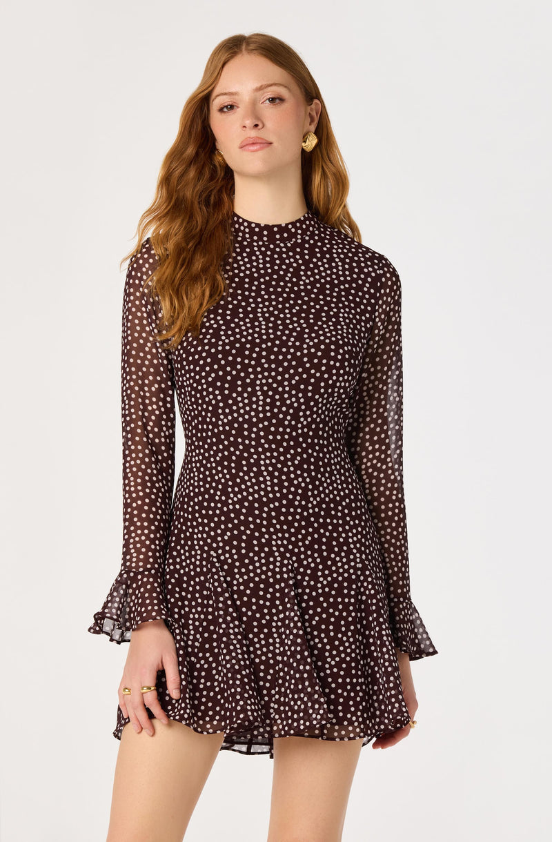Woman in a dark brown dress with white polka dots, long sleeves with ruffled cuffs.