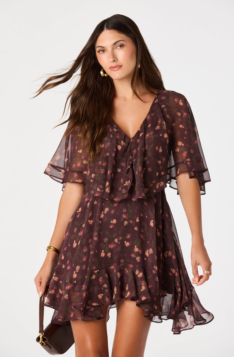 Woman in a dark floral dress with ruffles and sheer fabric, short sleeves.
