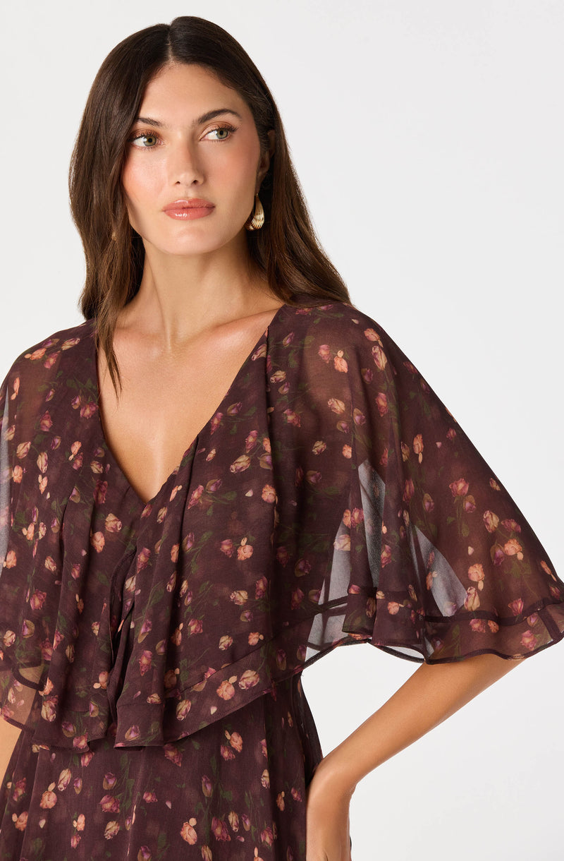 Woman in a sheer, floral dark brown dress with ruffled sleeves and a deep V neckline.