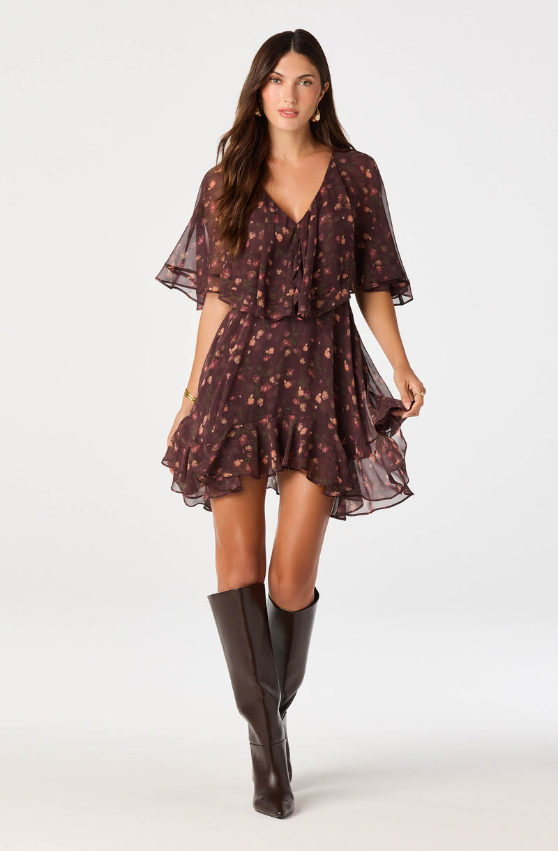 Woman in a dark floral dress with ruffled layers and sheer flutter sleeves, paired with tall black boots.