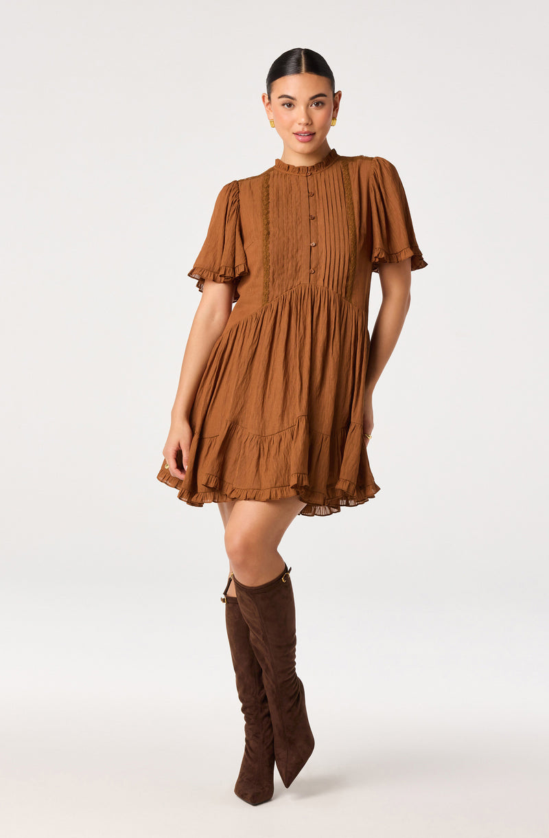 Brown pleated dress with puffed short sleeves and vertical striped details, paired with tall brown boots.