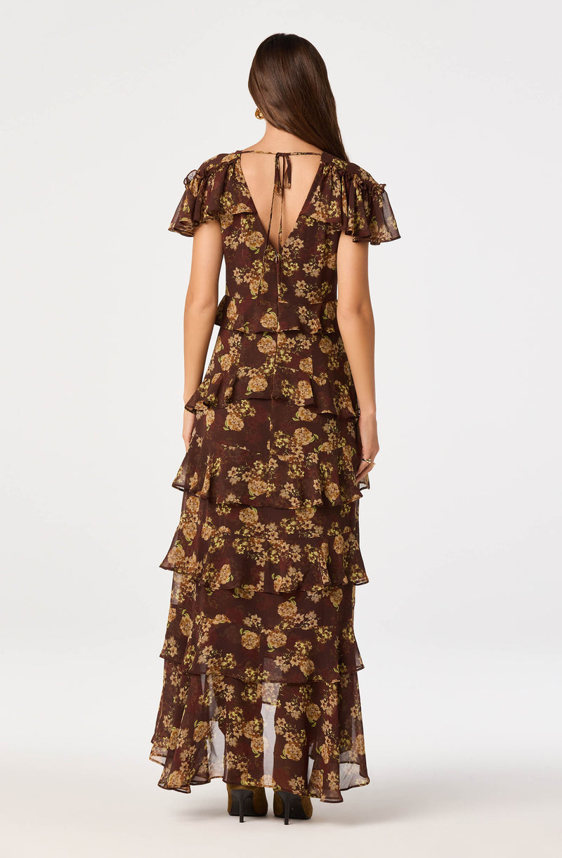 Woman wearing a dark floral tiered dress with ruffled sleeves and a tie-back detail at the neck.