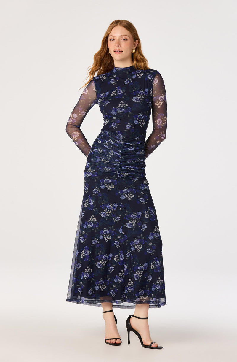 Woman wearing a long, navy blue floral dress with sheer, long sleeves and cutouts.