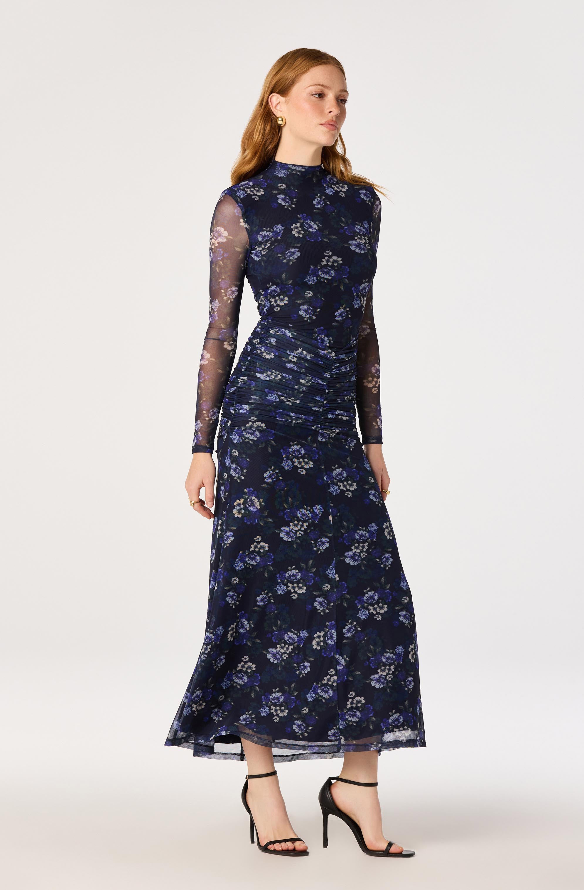 Woman in a long, navy floral dress with sheer long sleeves and black high heels.