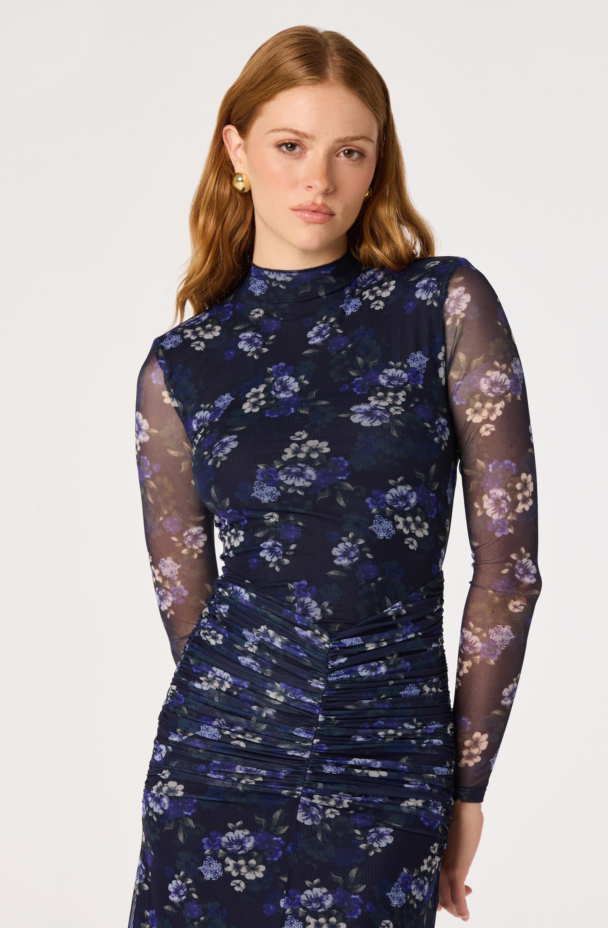 Woman wearing a dress with a high-neck lace top and a ruched floral skirt featuring purple, blue, and beige flowers.