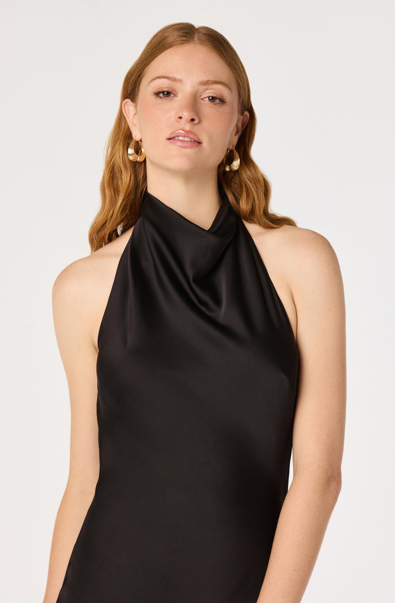 Woman in a black satin halter dress with gold hoop earrings.