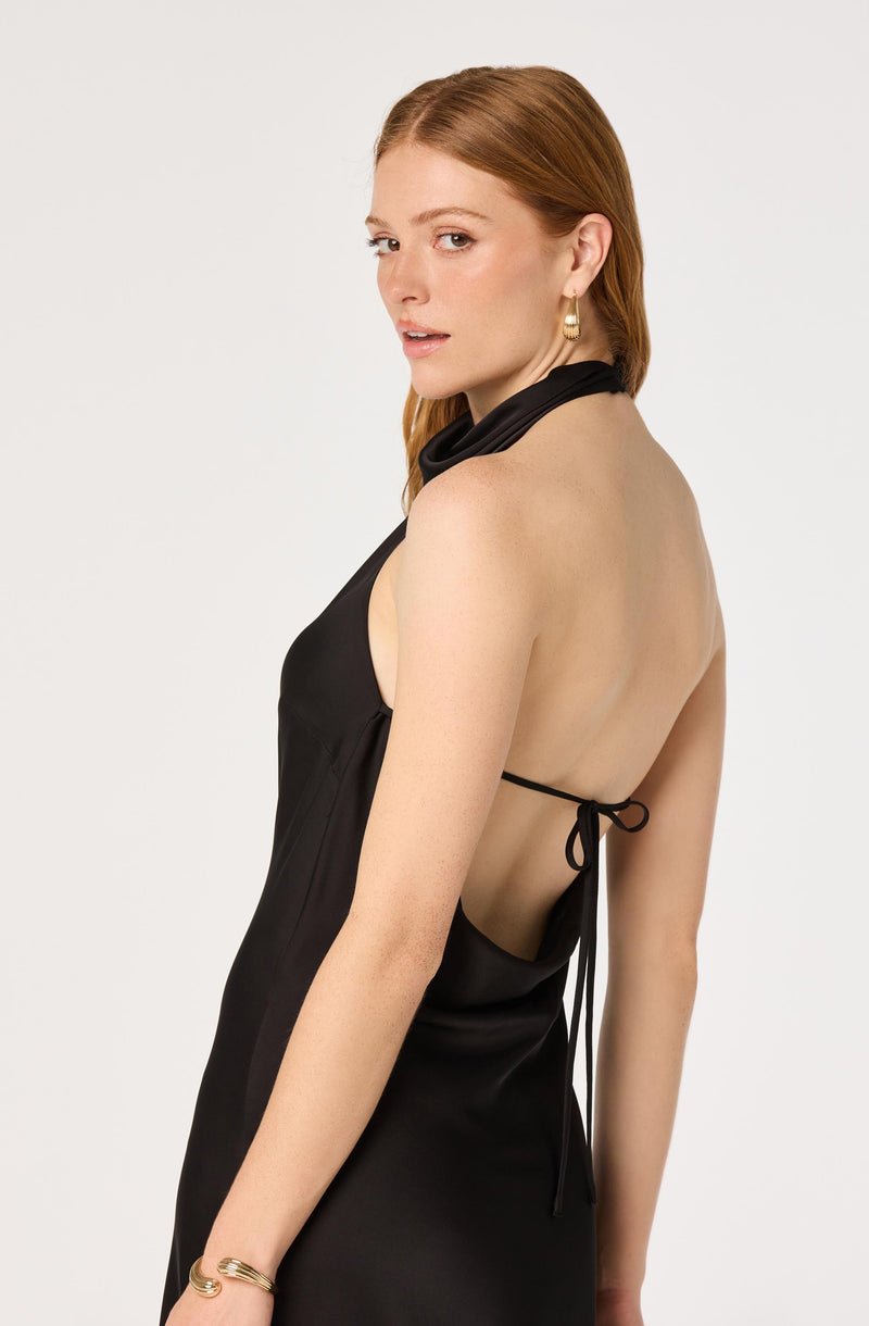 Woman in a black halter dress with open back and tie closure, wearing gold earrings.