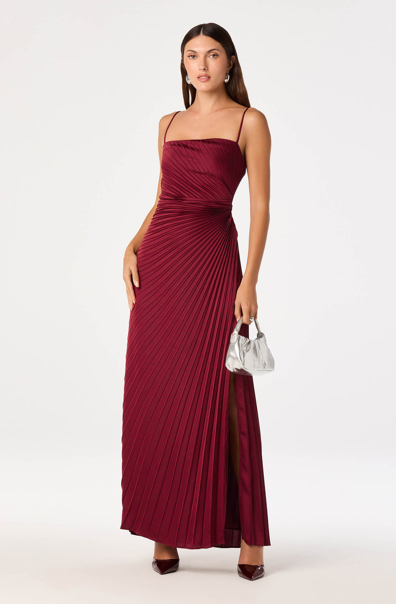 Woman in a long, red pleated gown with thin spaghetti straps, holding a silver clutch.