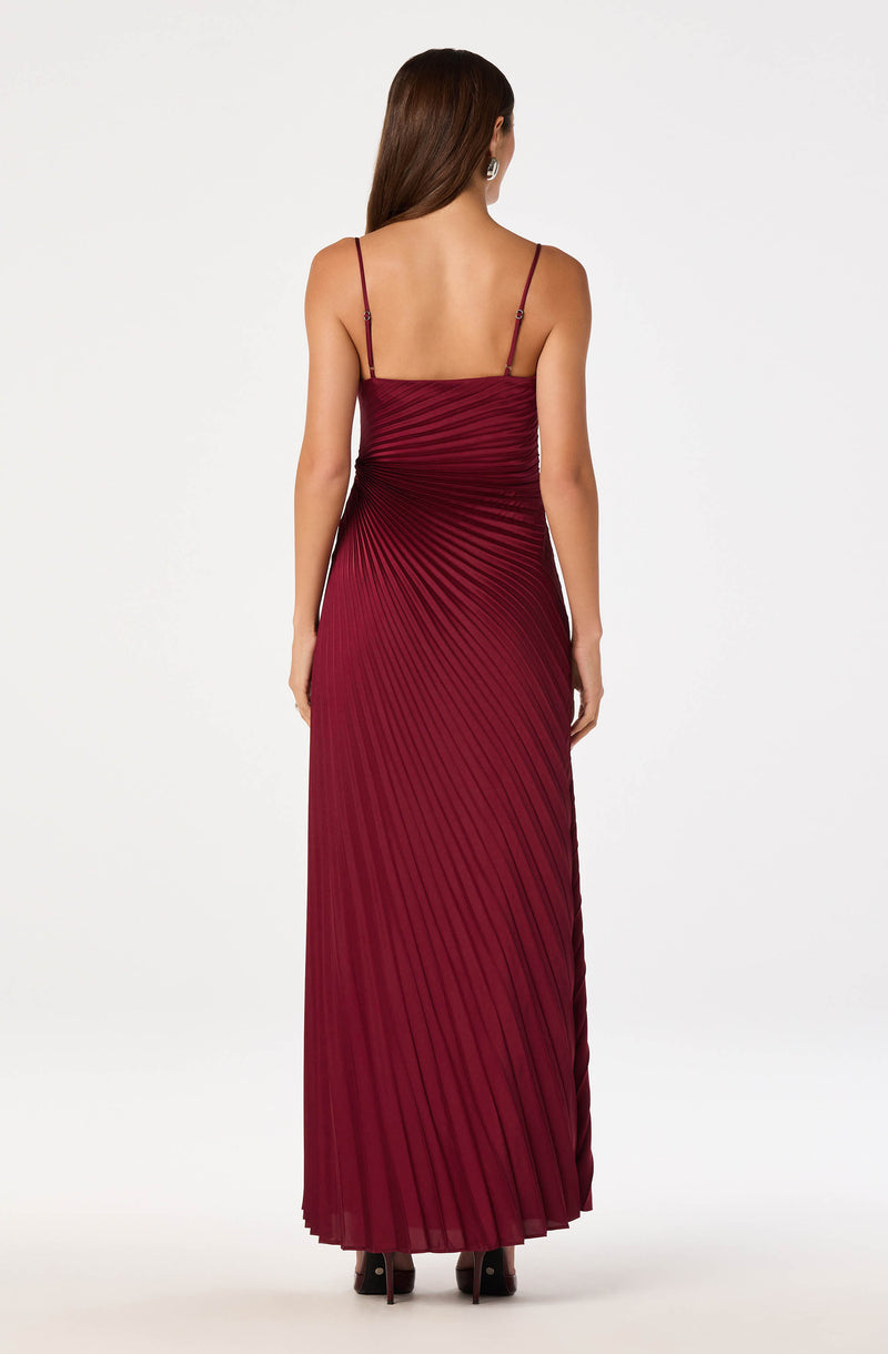 Woman in a long, burgundy pleated dress with thin spaghetti straps and open back.