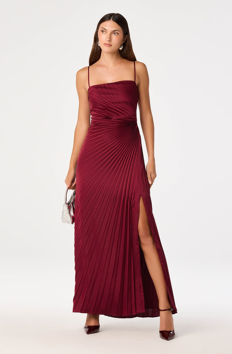 Woman in a floor-length burgundy pleated dress with thin straps and a thigh-high slit.
