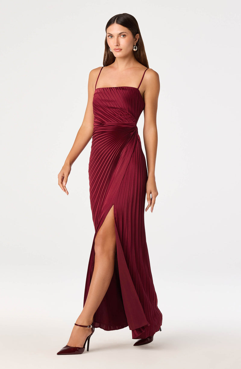 Women wearing burgundy pleated satin evening gown with spaghetti straps and a thigh-high slit.