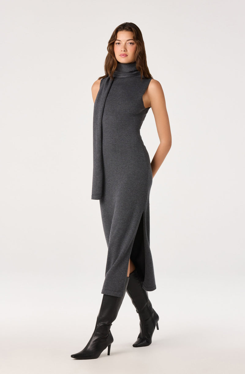 Woman in a sleeveless gray turtleneck dress with a matching scarf and black knee-high boots.
