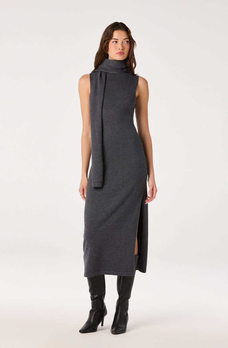 Woman in a sleeveless, high-neck gray dress with a slit and matching scarf, wearing knee-high black boots.