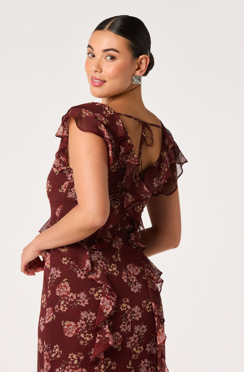 Woman wearing burgundy floral ruffled dress with open back and bow tie detail.